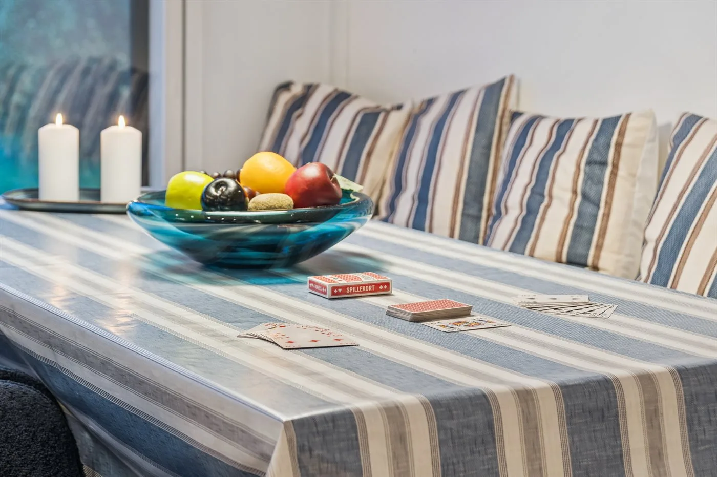A striped table with fruit and cards sits beside a cushioned bench.
