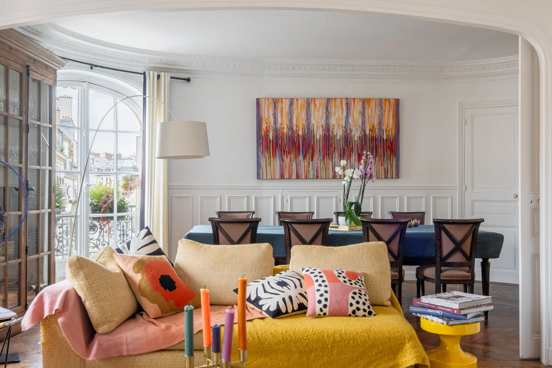 A bright living and dining room with colorful seating and a large abstract painting.
