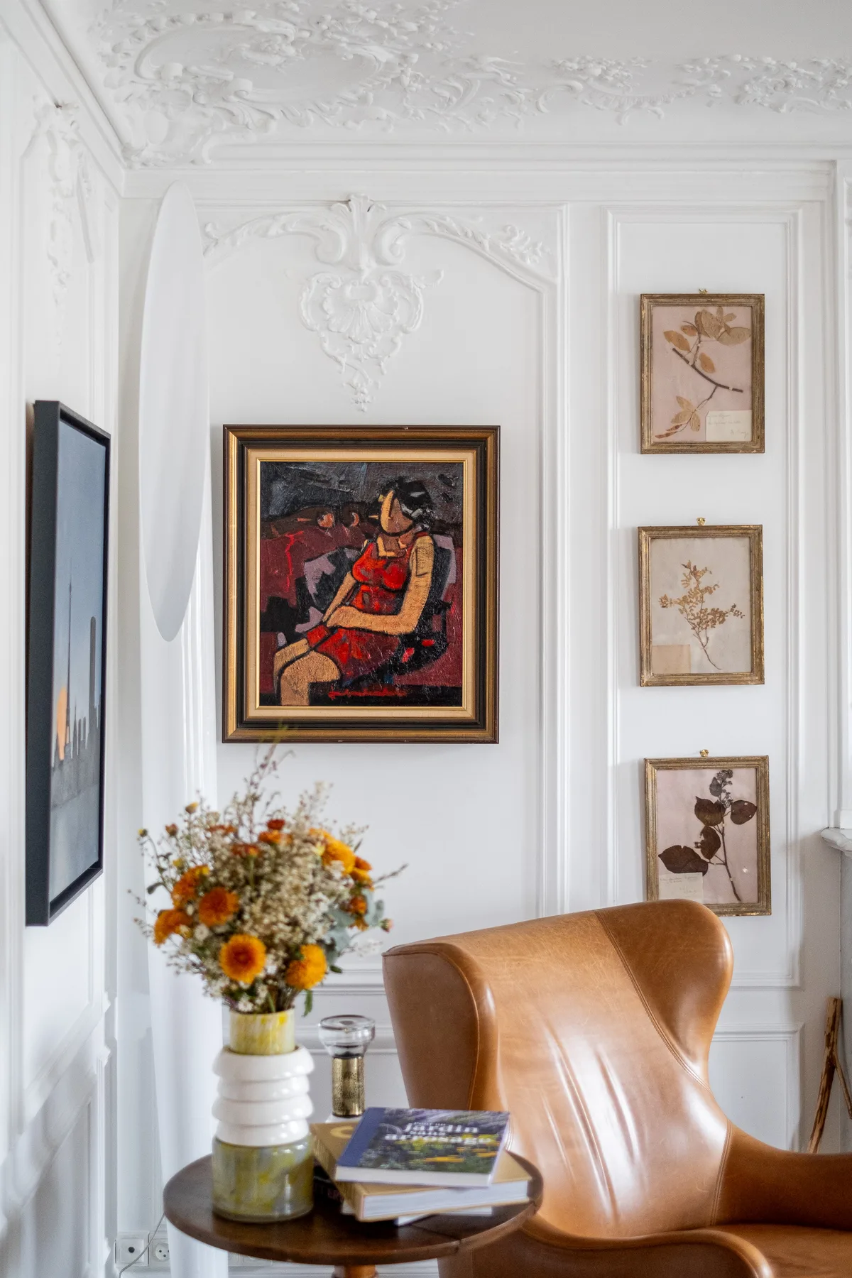 A bright sitting area features a leather chair, framed artwork, and flowers on a table.