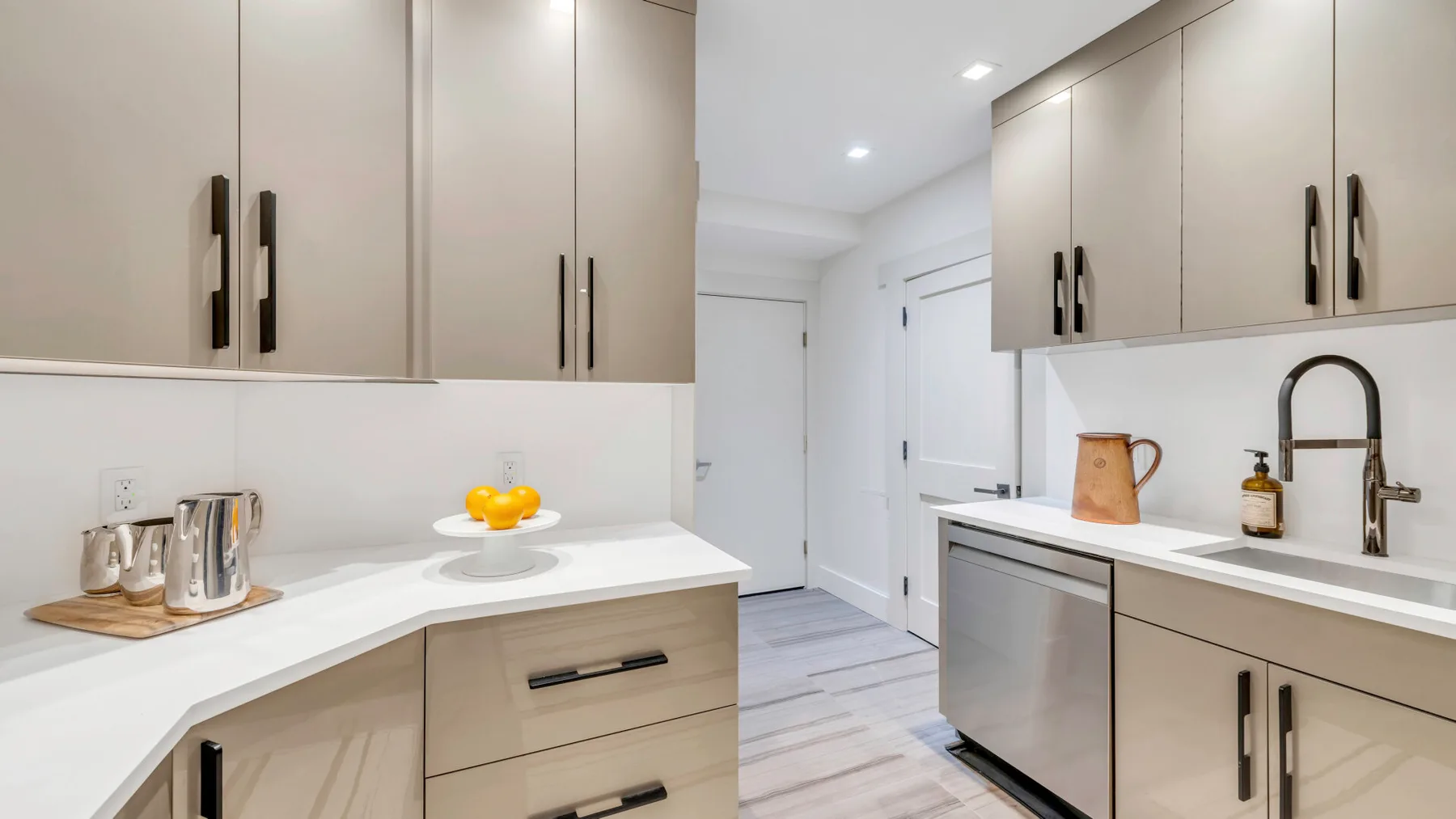 Una cocina luminosa con gabinetes claros, encimeras blancas y un fregadero.