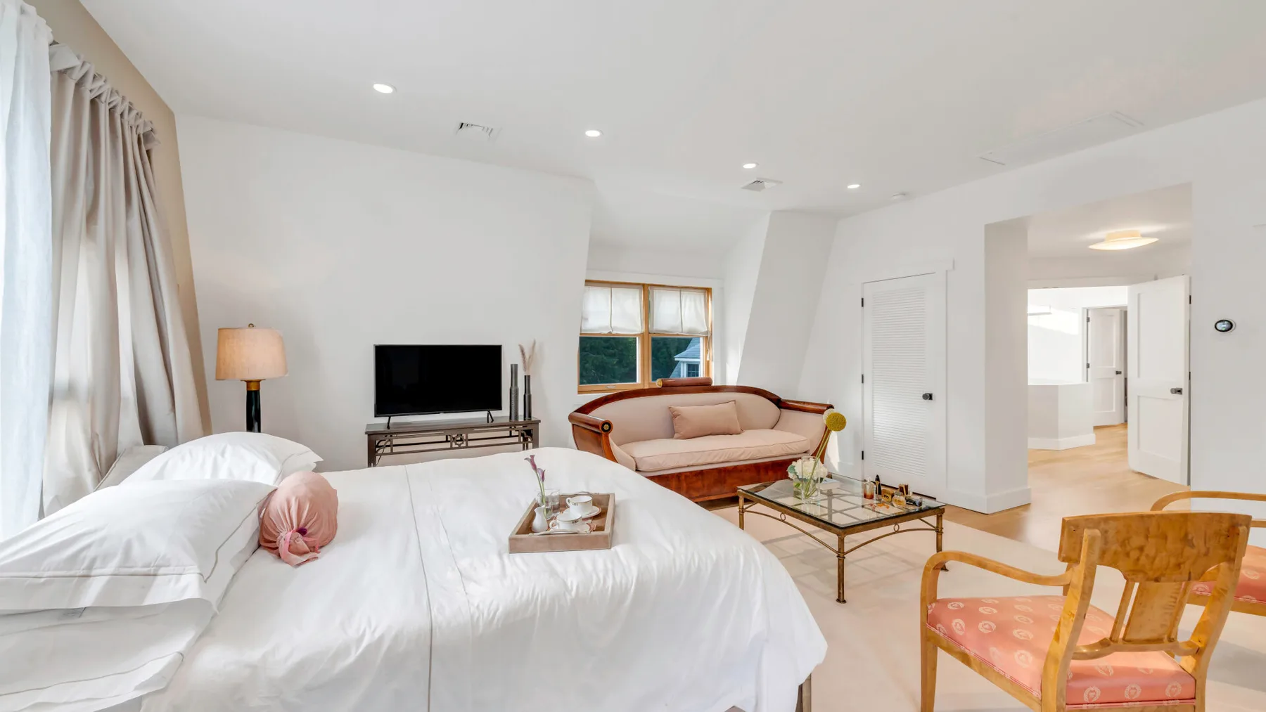 Un dormitorio luminoso con cama, zona de estar y televisor.