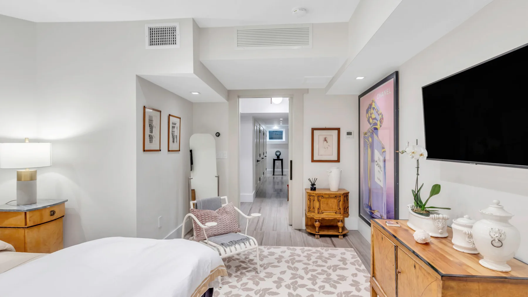 Un dormitorio luminoso con una cama grande, un televisor en la pared y una cómoda de madera.