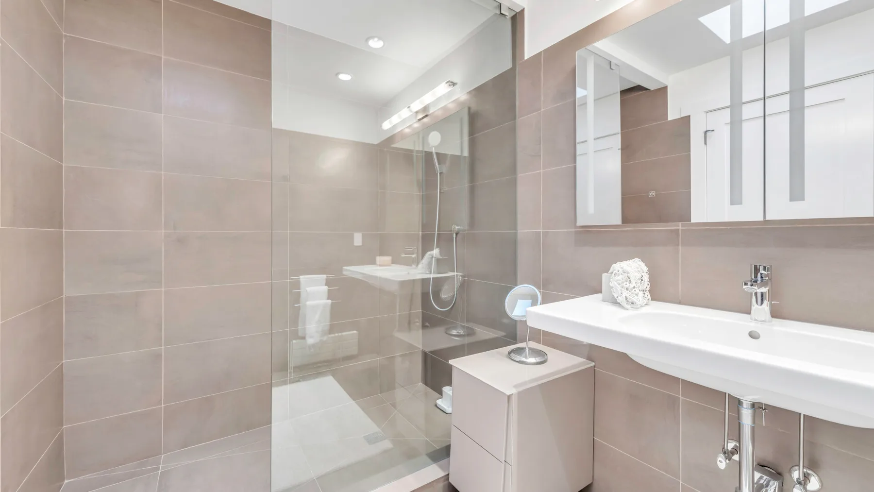 Un baño moderno con ducha de vidrio y un lavabo blanco alargado.