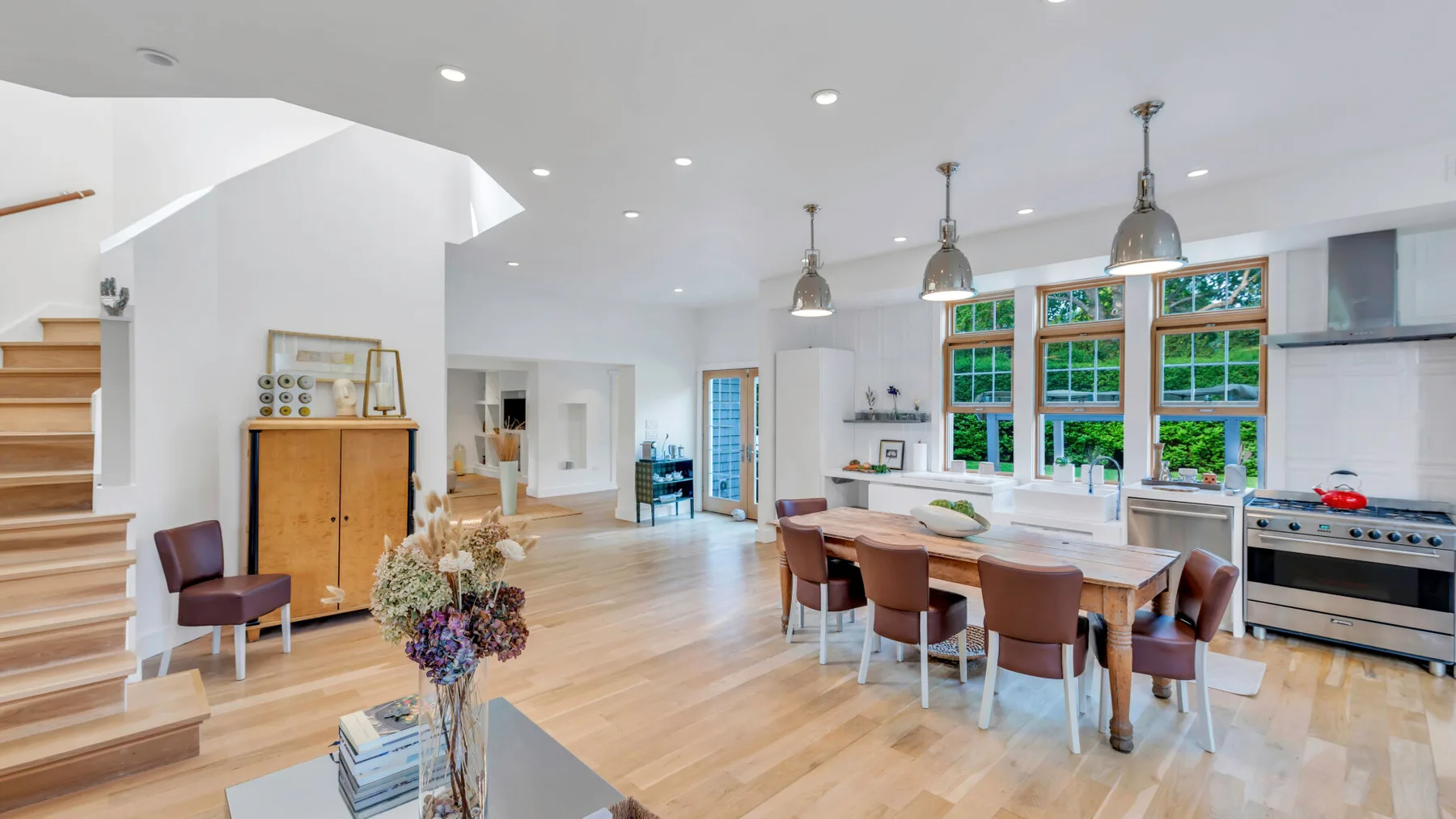 Una luminosa cocina y comedor de planta abierta, con grandes ventanas y una mesa larga.