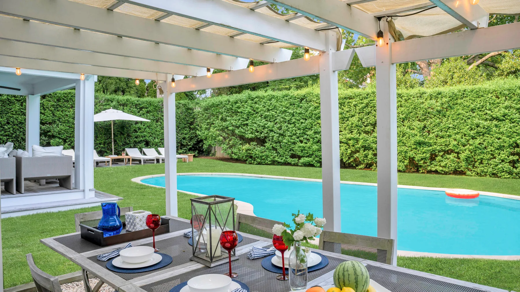 Una zona de comedor cubierta da a una piscina y un césped verde.