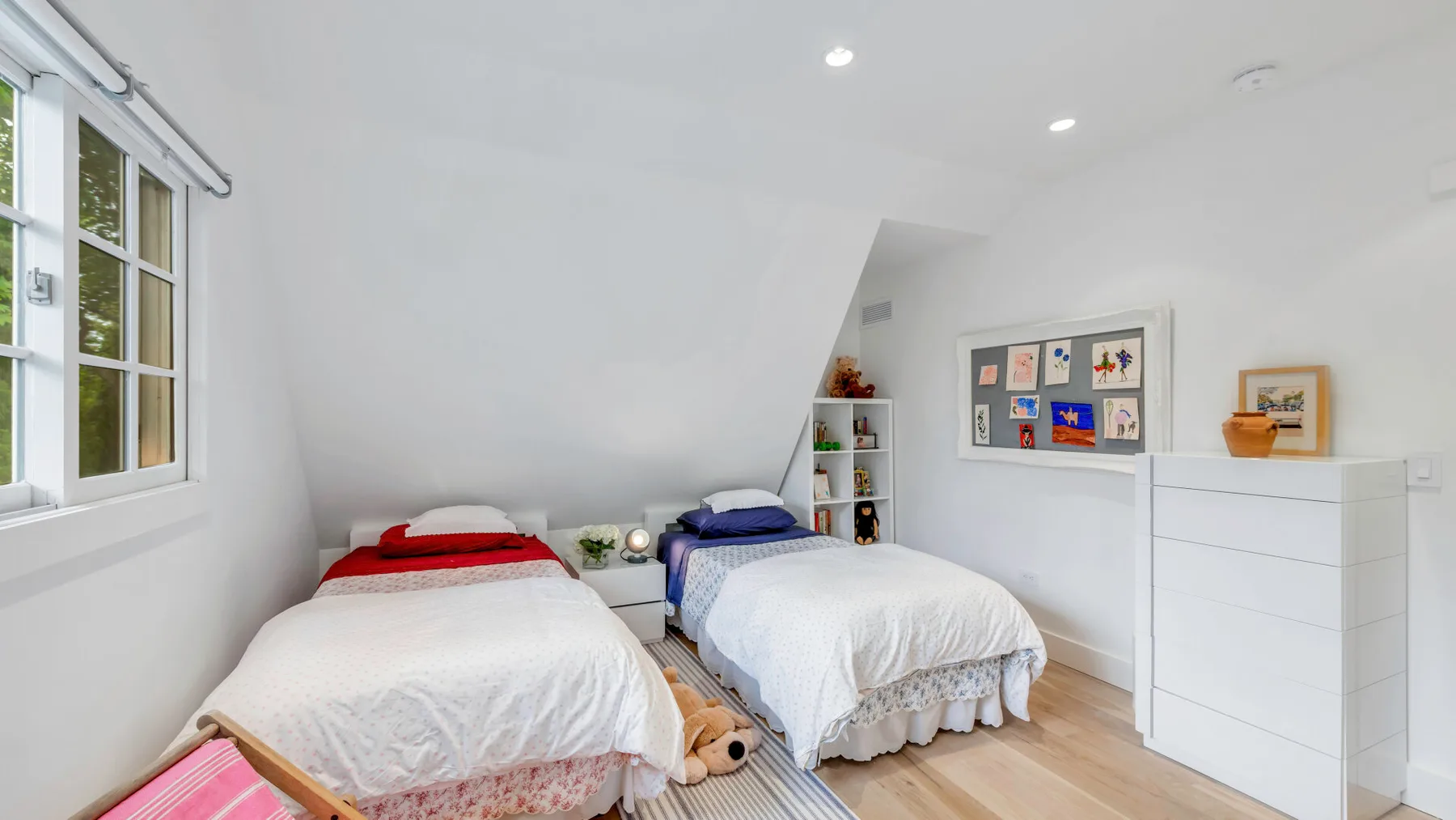 Un dormitorio luminoso con dos camas y una ventana en la pared izquierda.