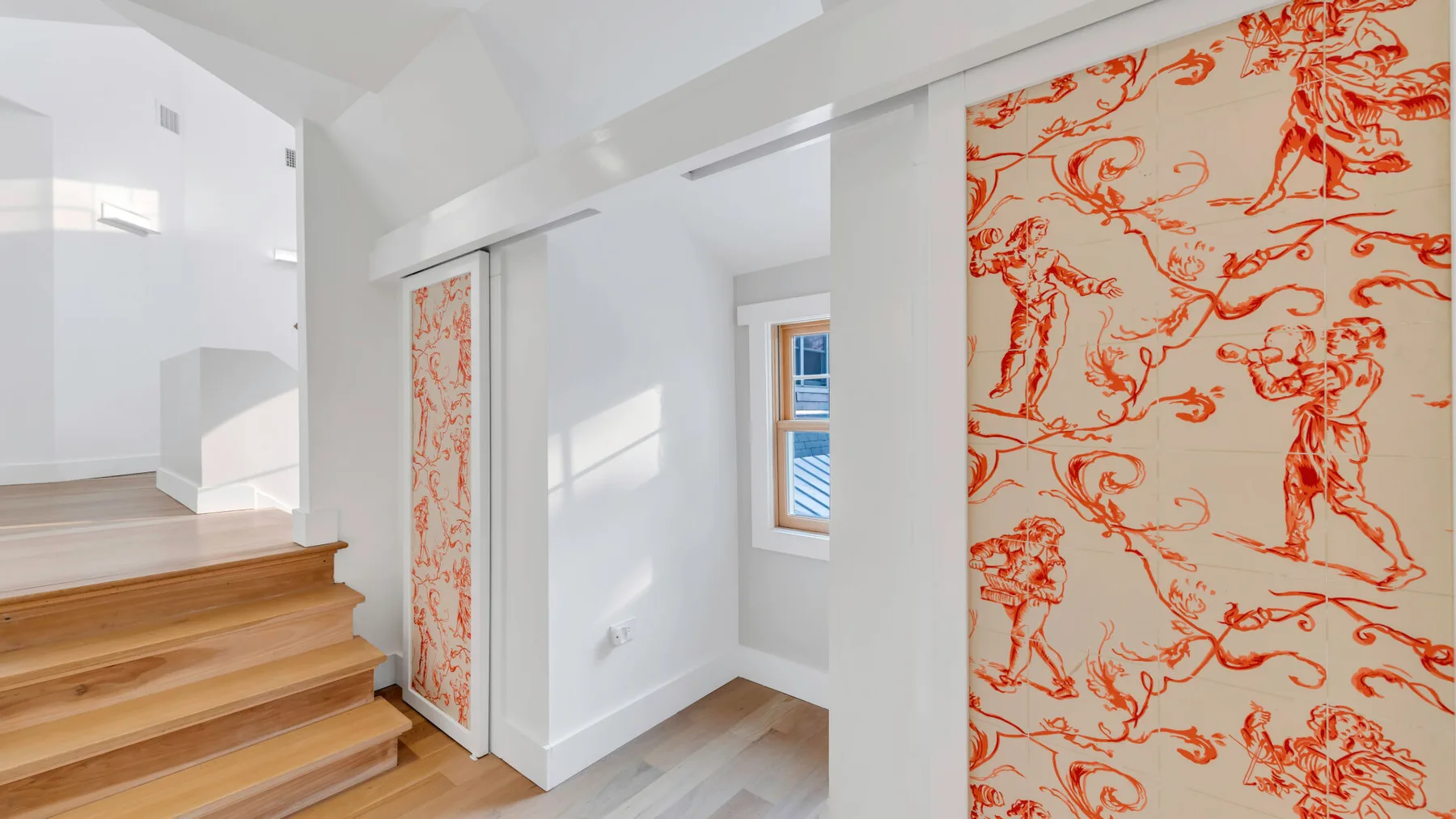 Una escalera luminosa con peldaños de madera y paneles decorativos de pared con motivos rojos.