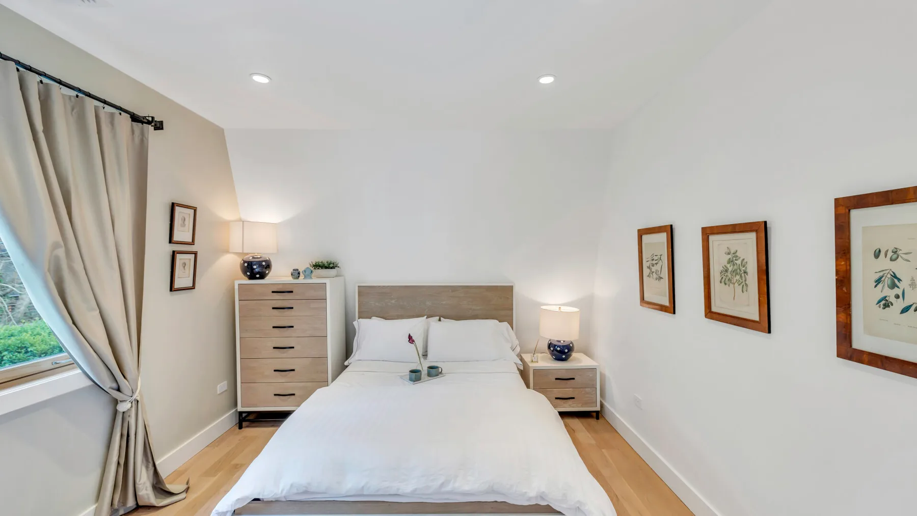 Un dormitorio luminoso con una cama bien tendida y cuadros en las paredes.