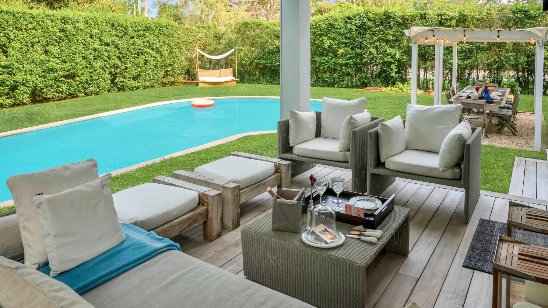 Un patio amueblado da a una piscina y un jardín frondoso.