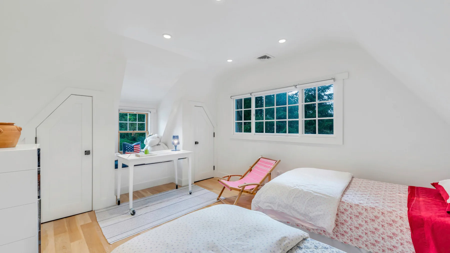 Un dormitorio luminoso con cama, sillón rosa y escritorio junto a una ventana grande.