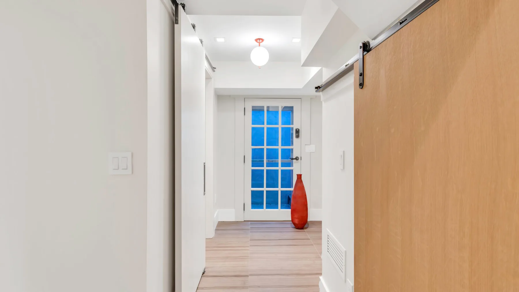 Un pasillo luminoso con una puerta corrediza de madera y una puerta de paneles azules al fondo.