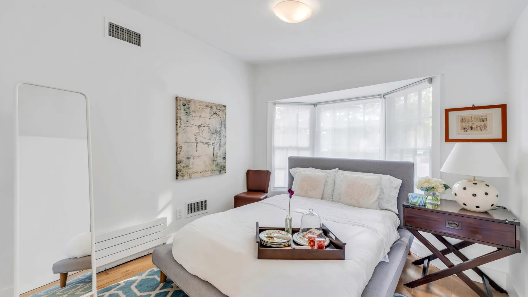 Un dormitorio luminoso con una cama, una mesa auxiliar y ventanas amplias.