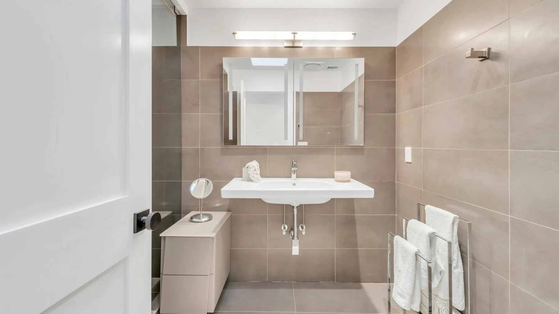 Un baño con azulejos, lavabo, armario con espejo y toallas colgadas al lado.