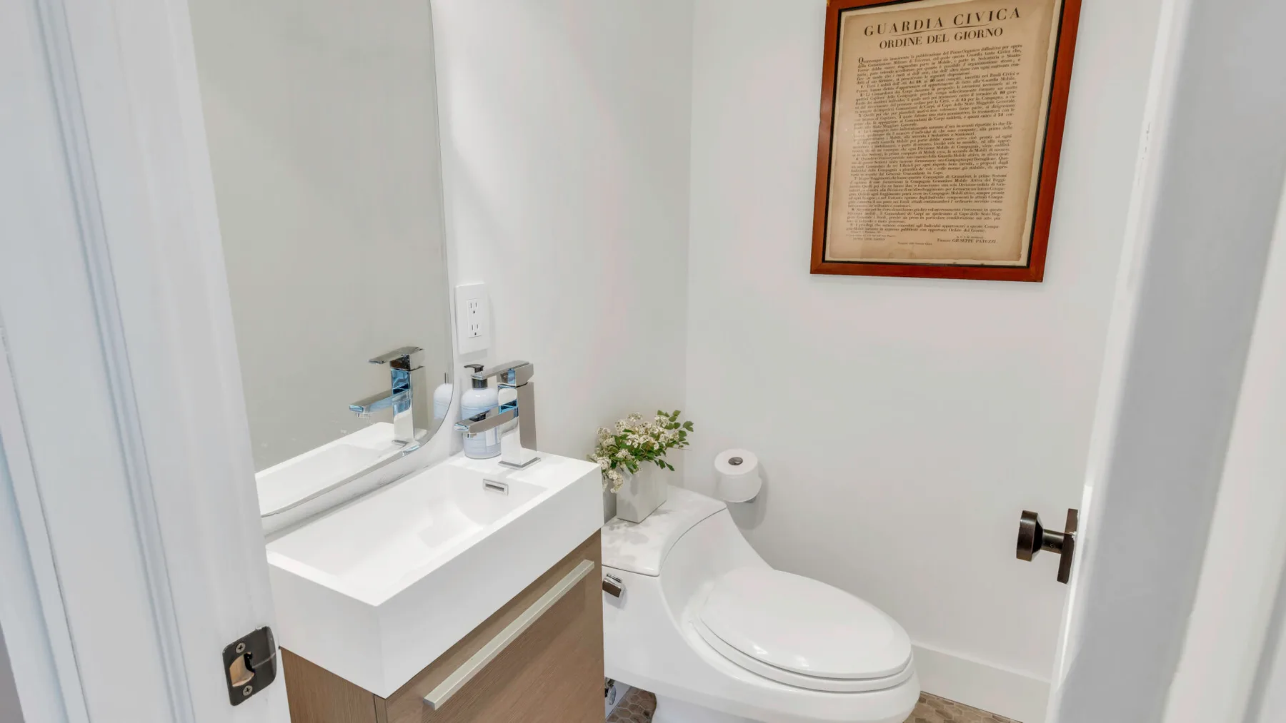 Un baño luminoso con lavabo, inodoro y un cuadro enmarcado en la pared.