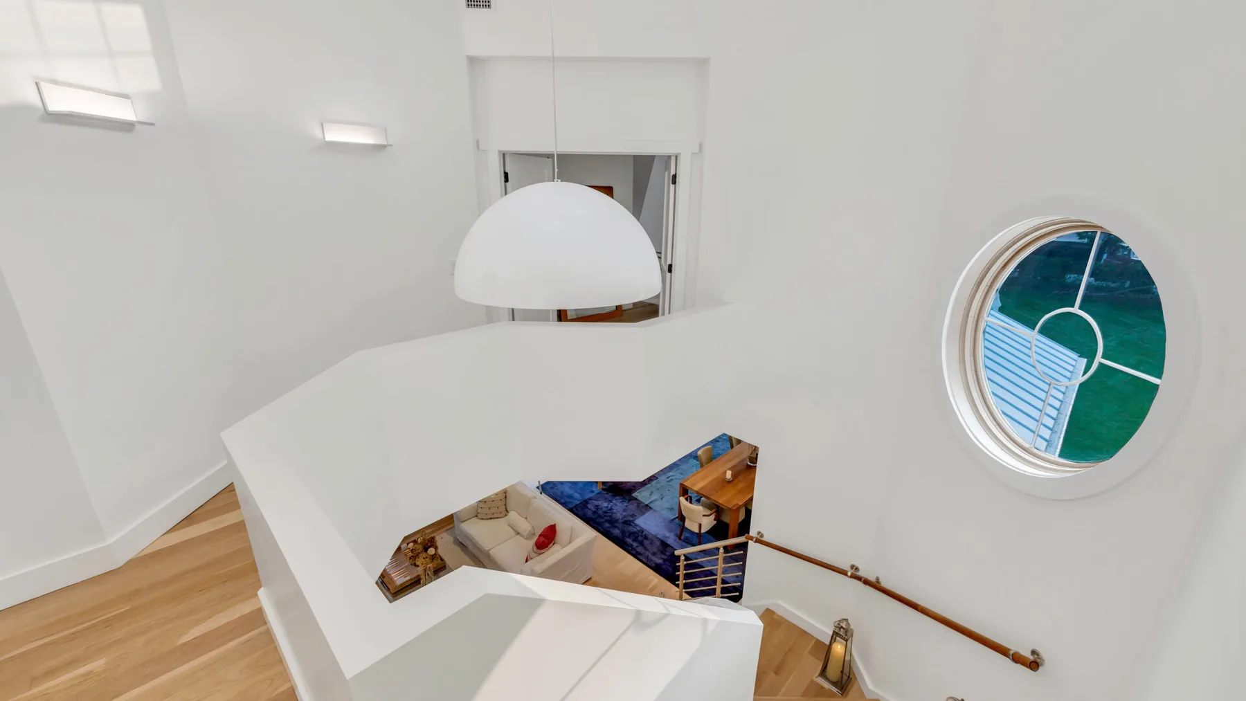 Una escalera interior luminosa con una barandilla blanca curva y una ventana redonda.