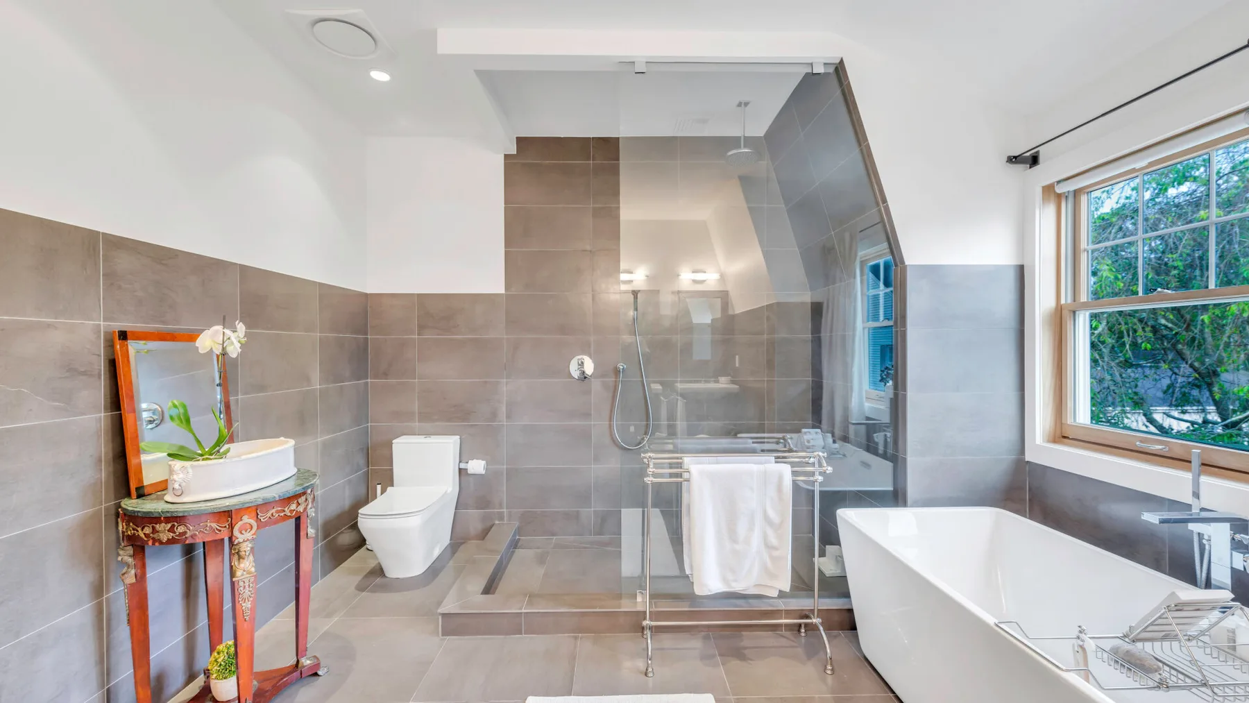 Un baño moderno con ducha de vidrio, bañera y una ventana grande.