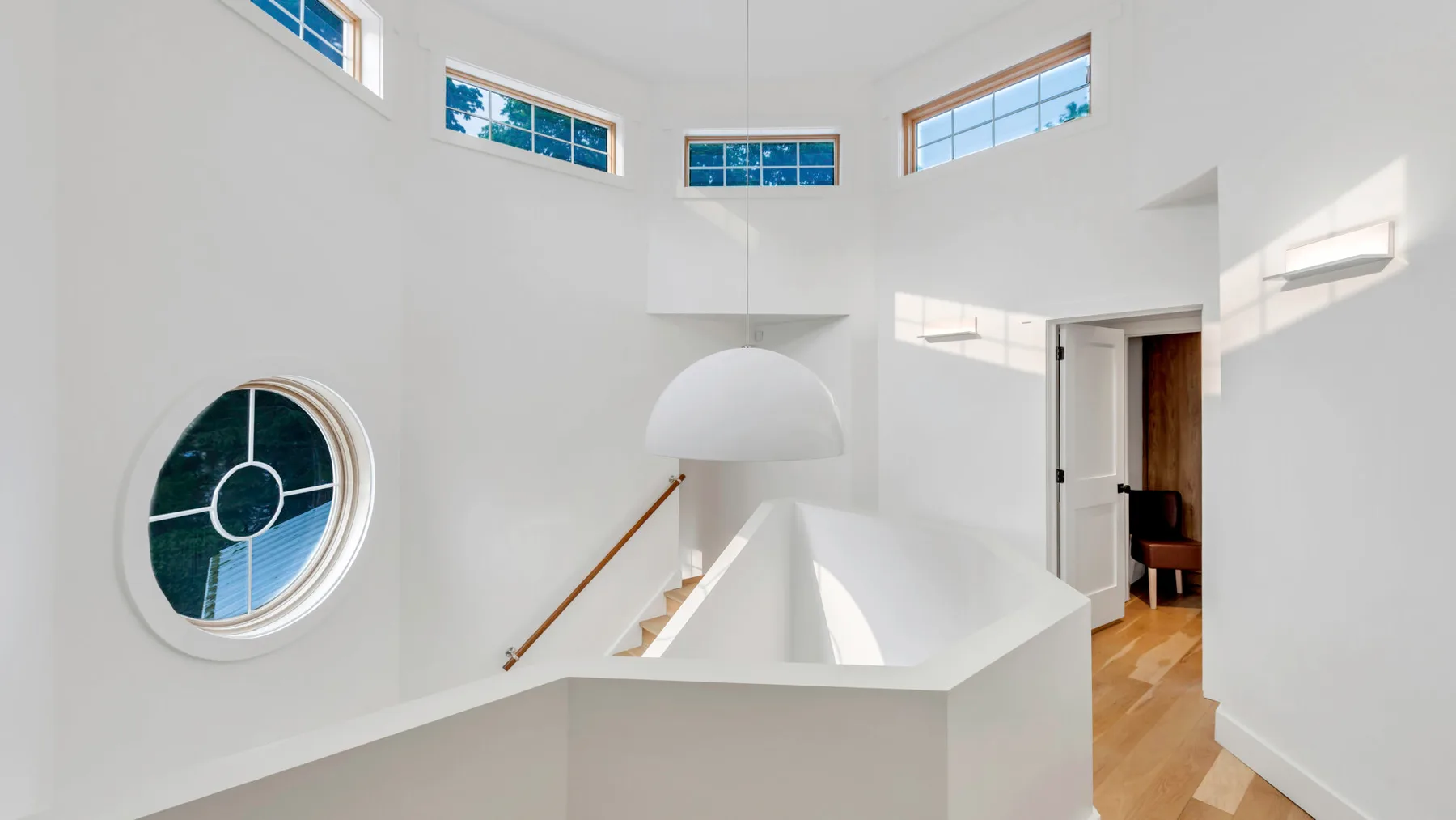Un interior blanco y luminoso con una ventana circular y una escalera abierta.