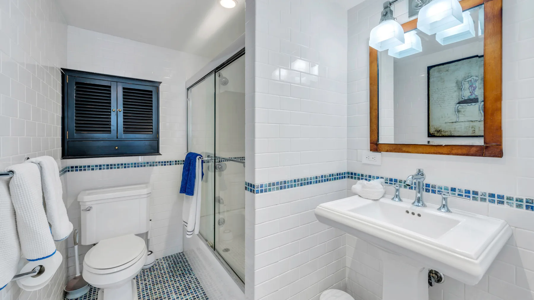 Un baño alicatado con inodoro, ducha de vidrio y lavabo bajo un espejo.
