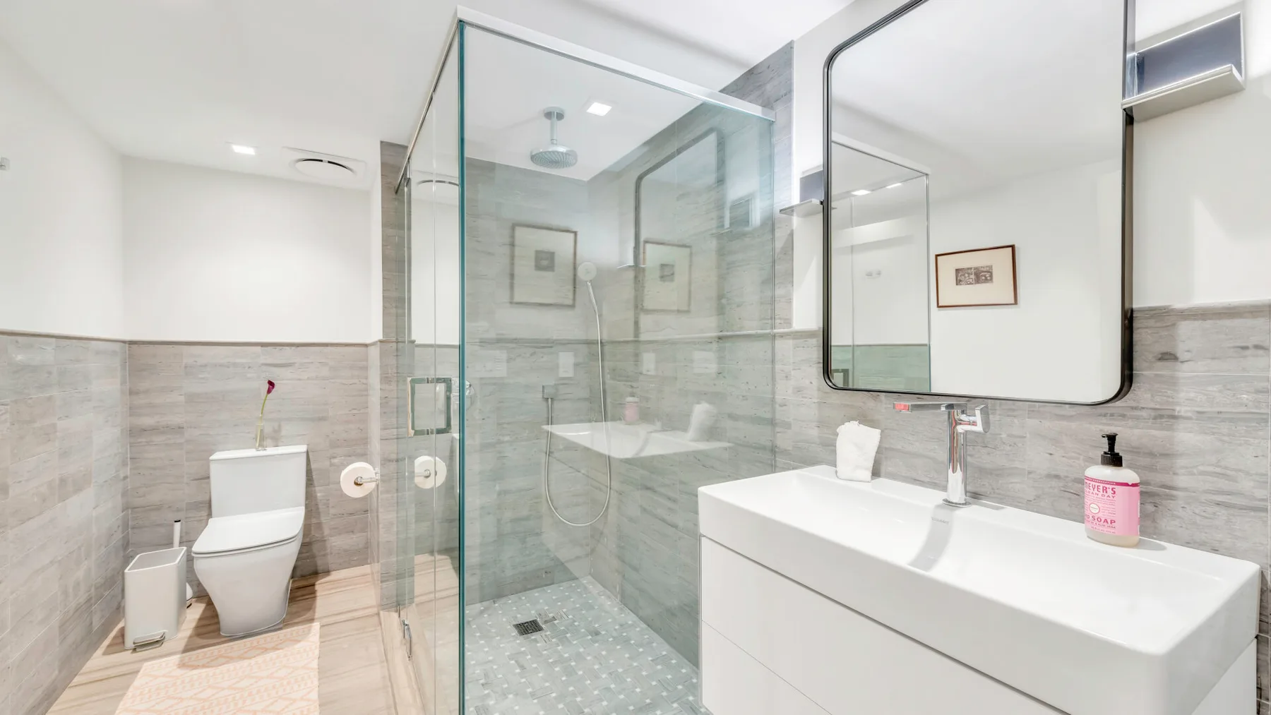 Un baño luminoso con ducha de vidrio, inodoro y lavabo.