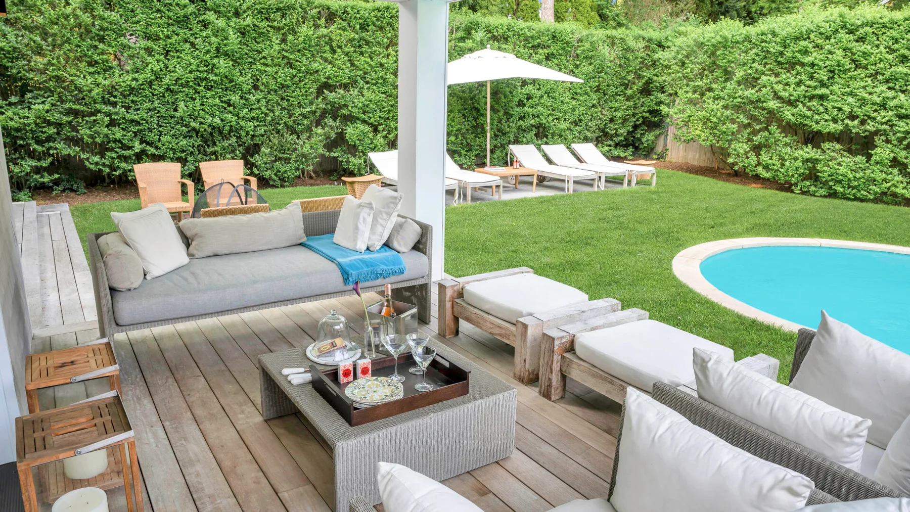Un patio al aire libre con asientos acolchados, una mesa baja y una piscina.