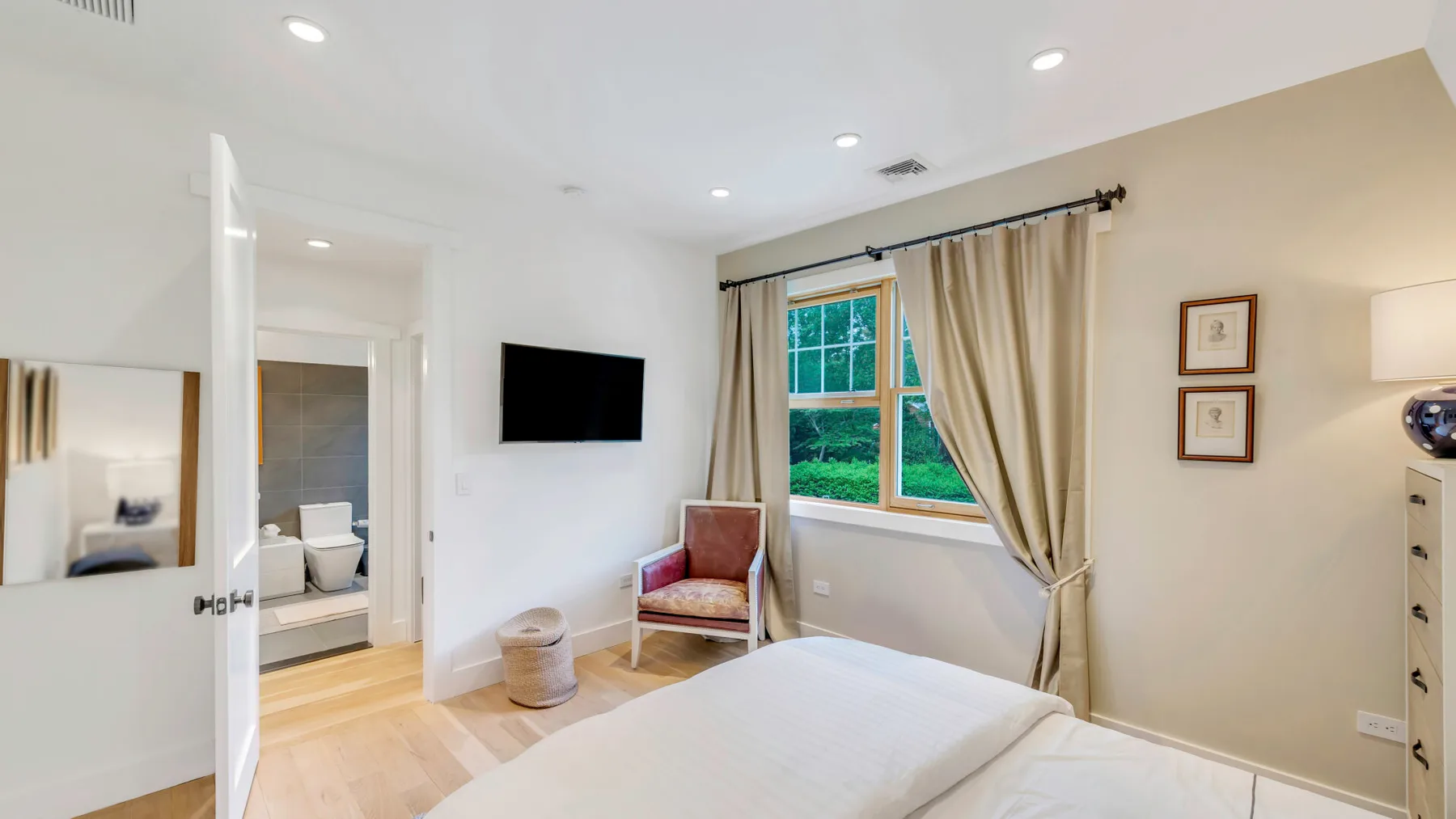 Un dormitorio luminoso con una cama, un sillón y una ventana con vistas a vegetación.