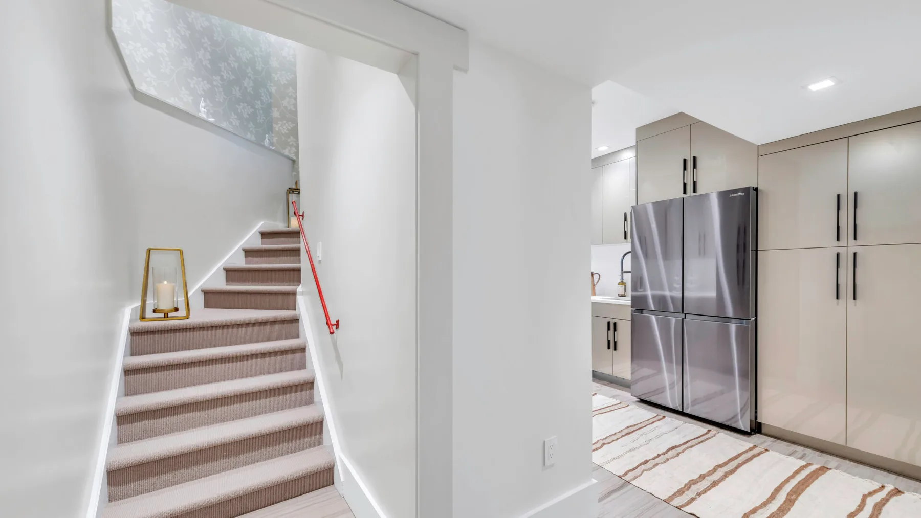 Una cocina luminosa junto a una escalera, con gabinetes claros y un refrigerador de acero inoxidable.