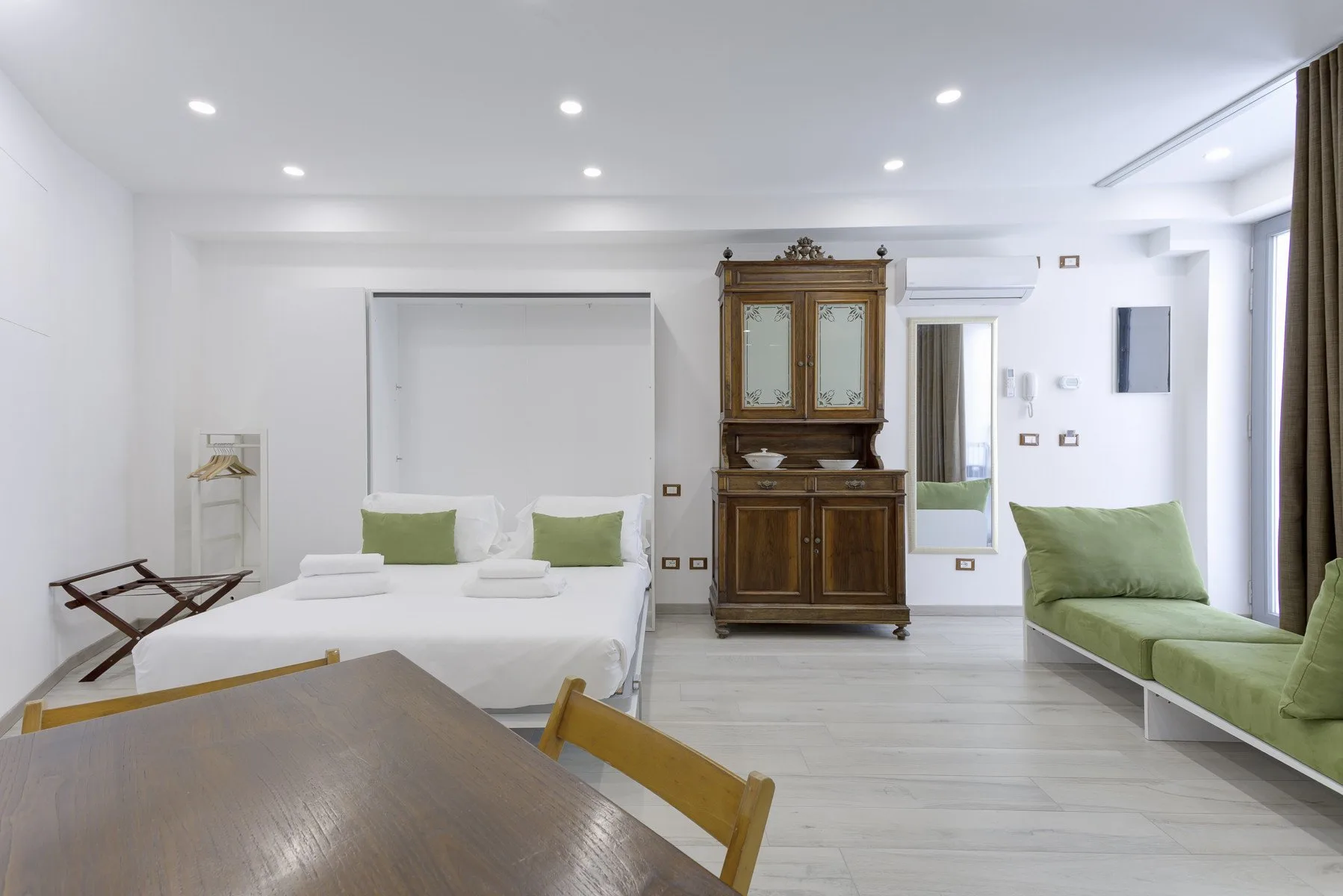 Un dormitorio luminoso con una cama, un mueble de madera y asientos verdes.