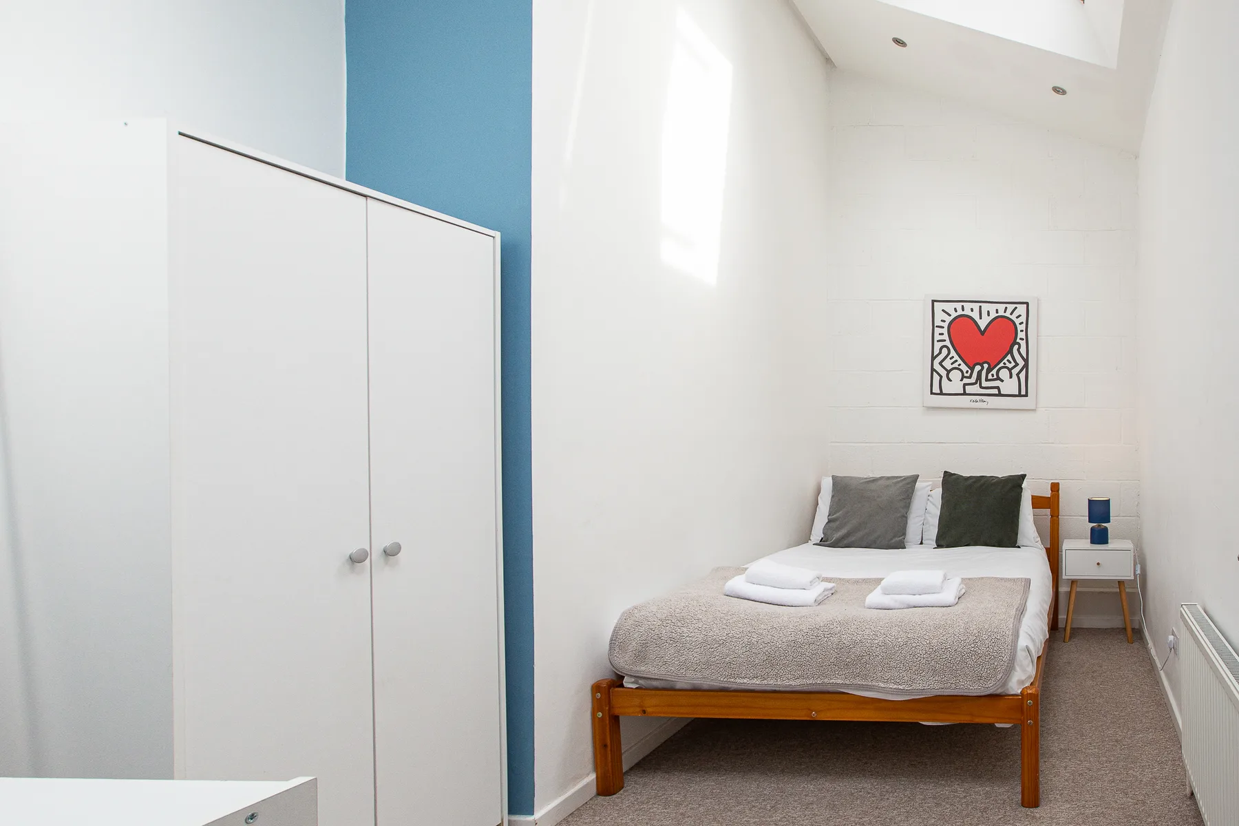 A bright bedroom with a bed beneath framed heart artwork.
