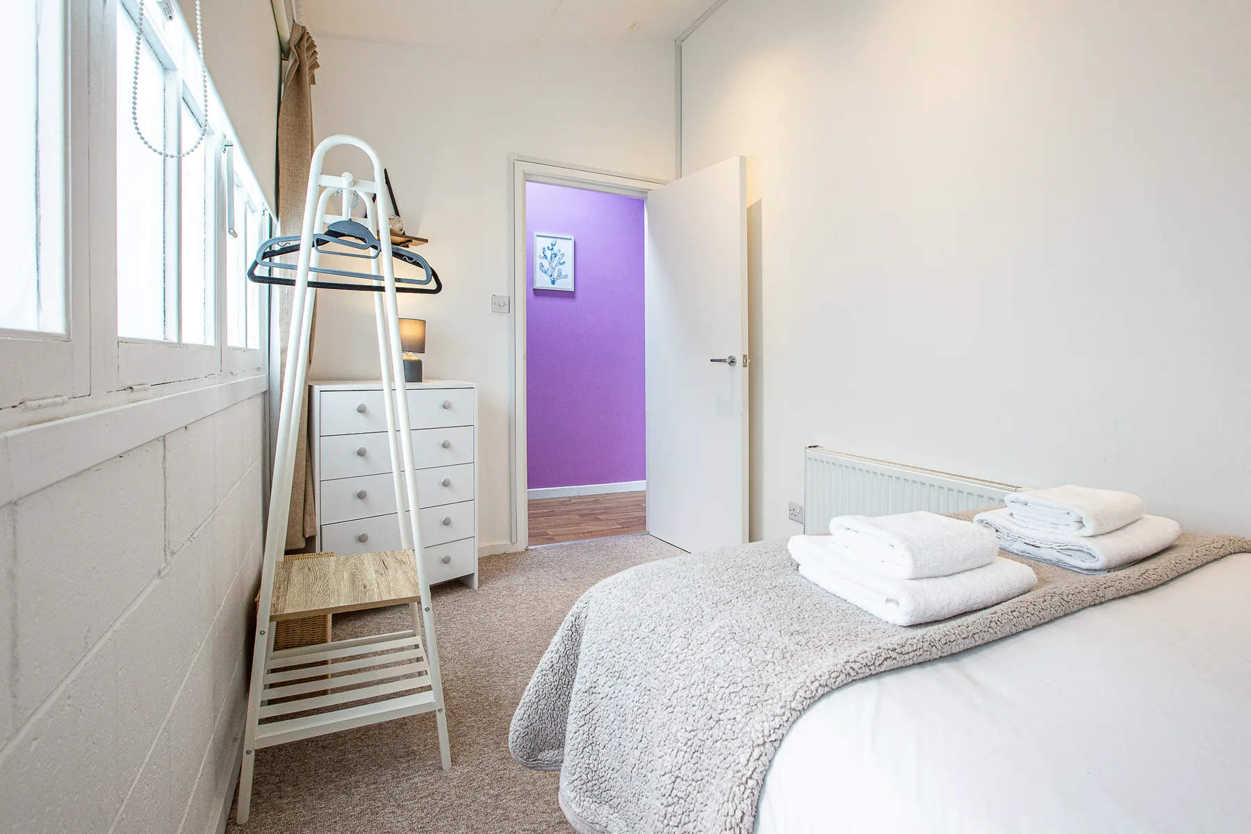 A bright bedroom with a bed, dresser, and open doorway.