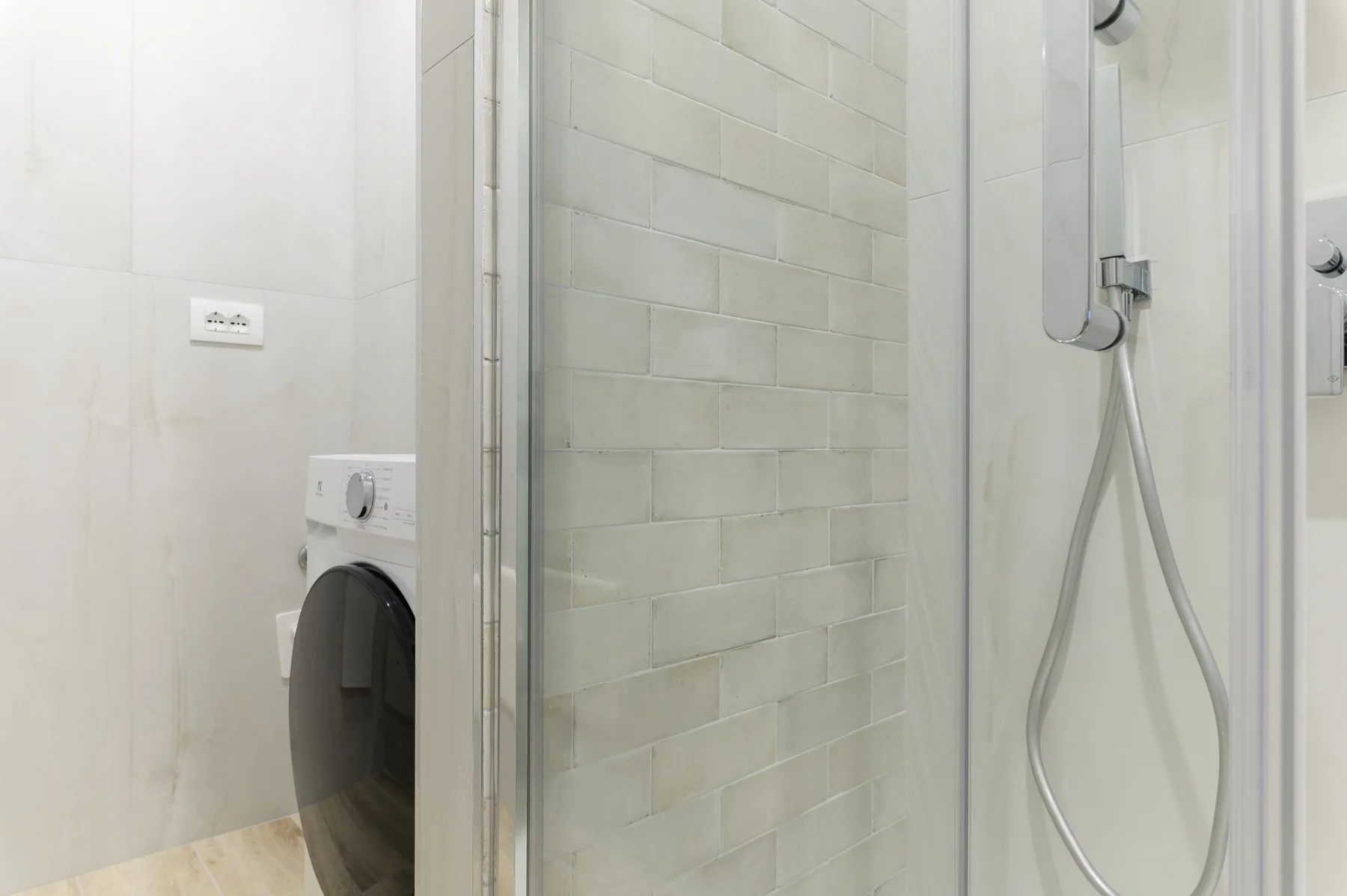Un baño con una lavadora junto a una ducha con azulejos.