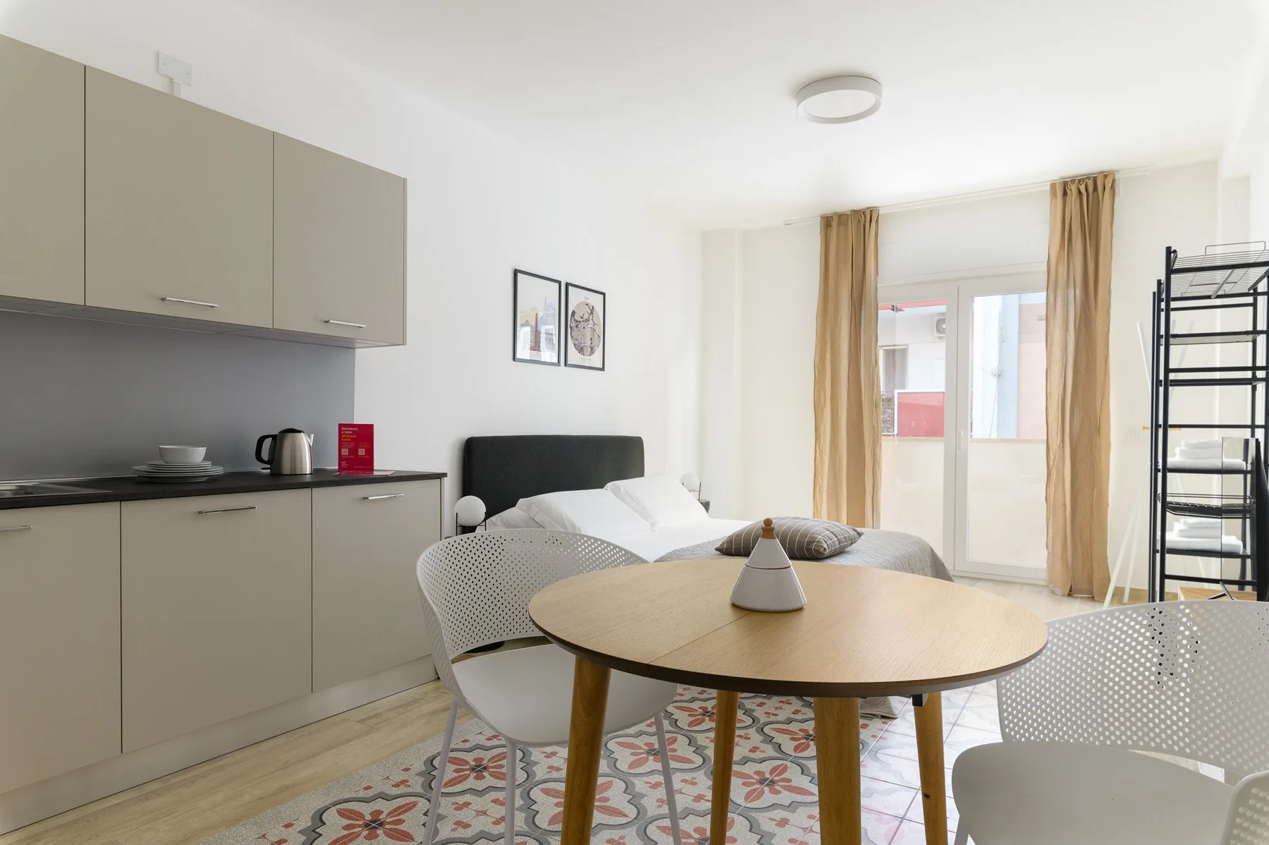A bright studio room with a bed, kitchenette, and round table.