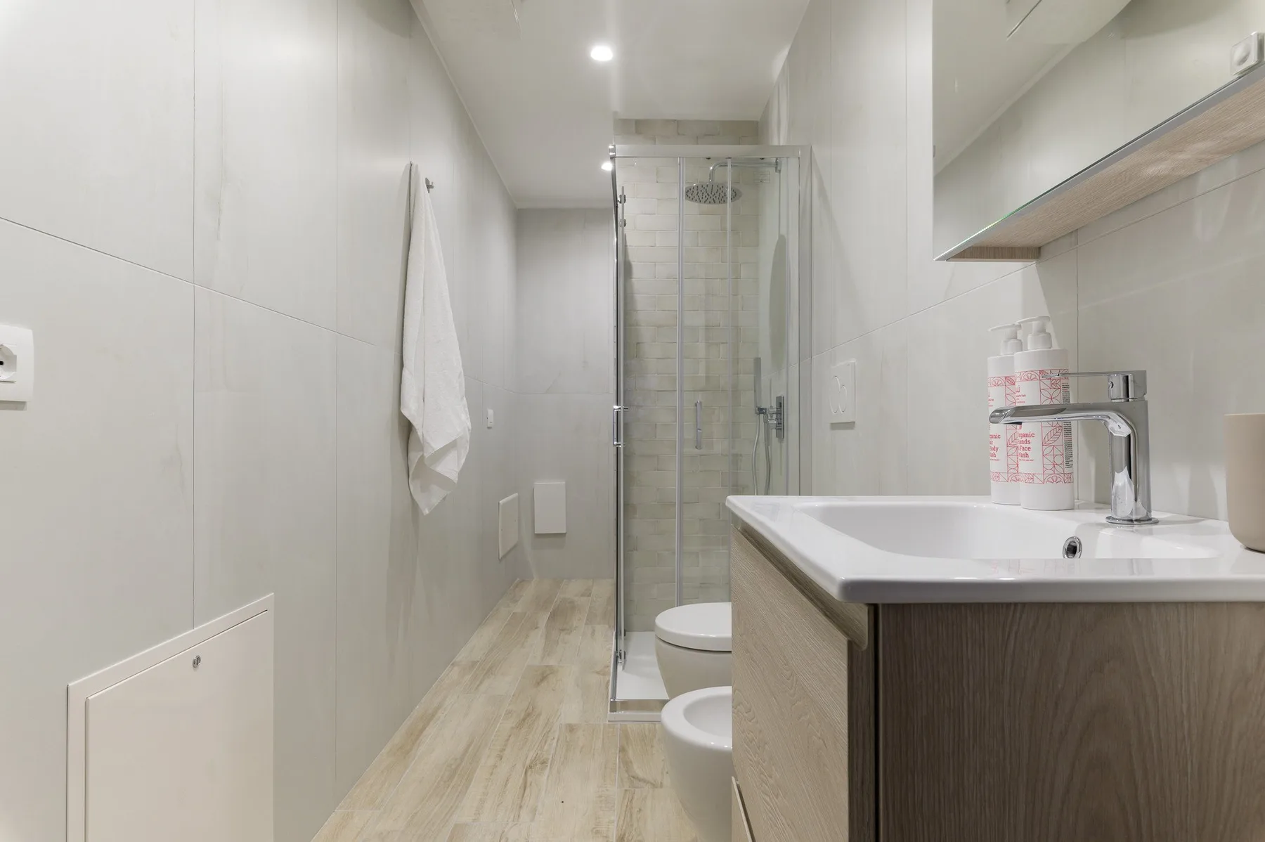 Un baño estrecho con una ducha de vidrio y un lavabo con mueble.