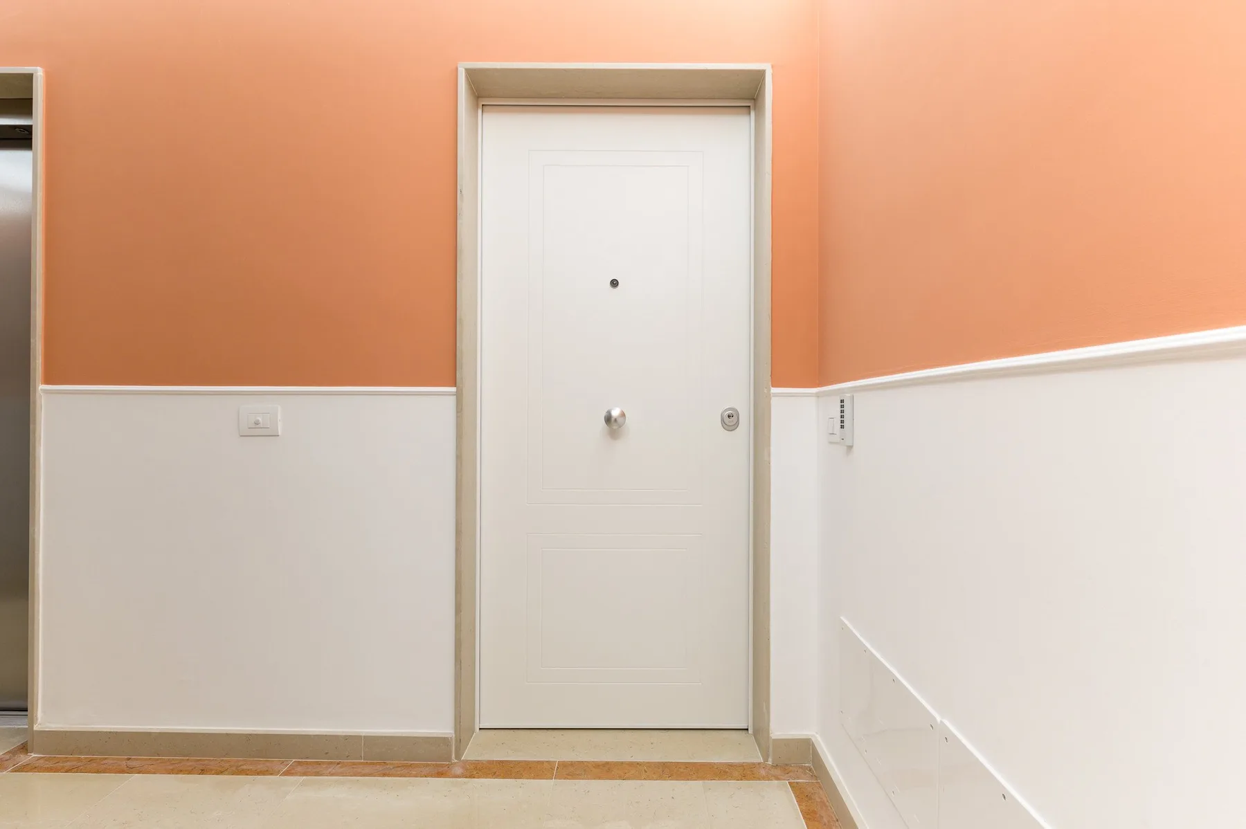 Una puerta blanca está en un pasillo con paredes superiores color durazno y paredes inferiores blancas.