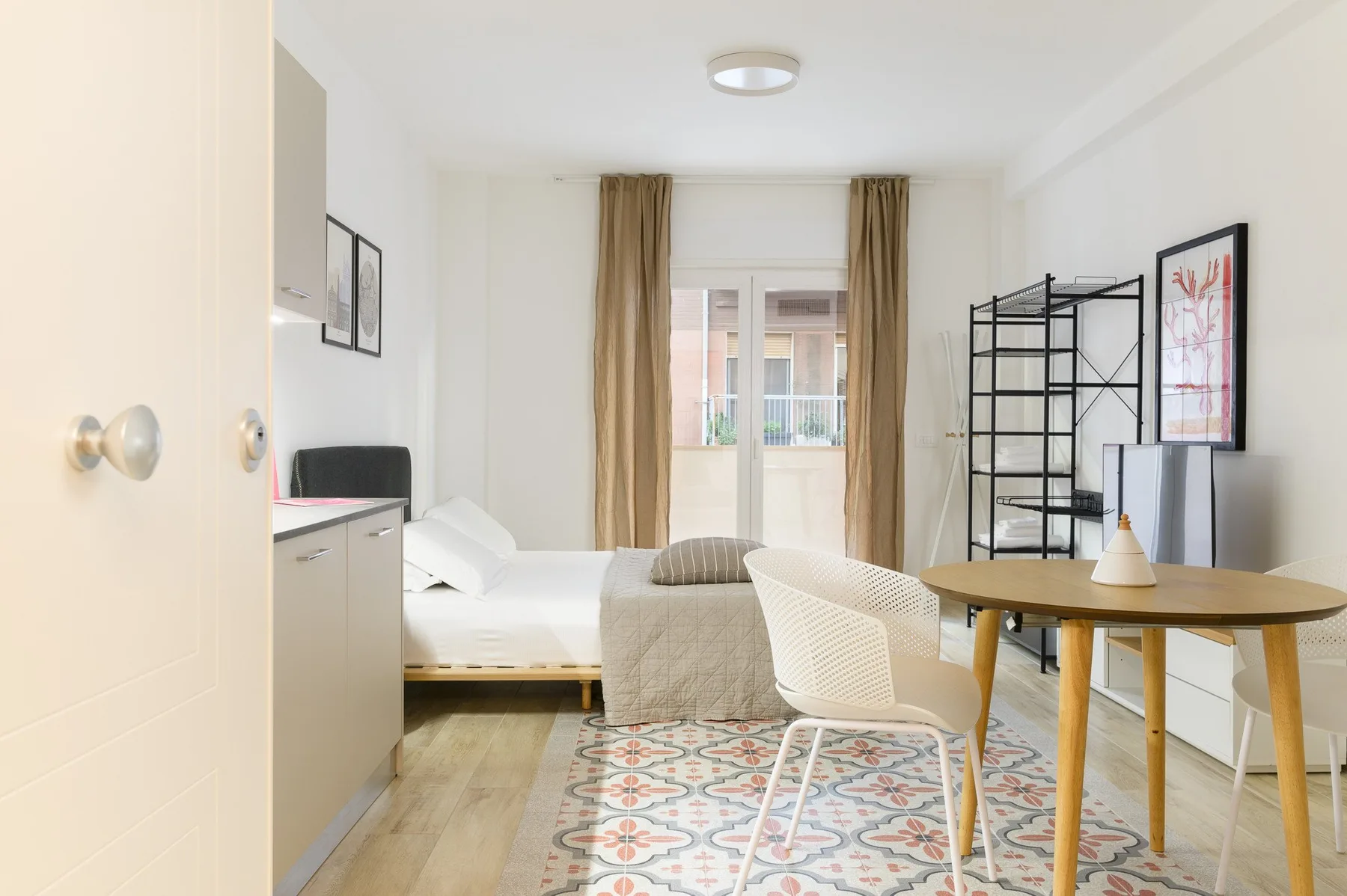 A bright bedroom with a bed, a small dining table, and a window with curtains.