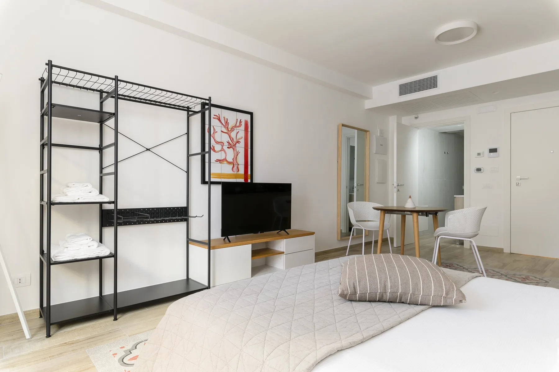Un dormitorio luminoso con una cama baja, estanterías abiertas y una pequeña zona de comedor.