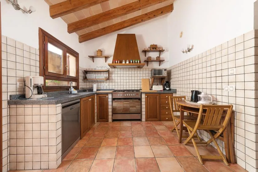 A tiled kitchen with wooden cabinetry, exposed ceiling beams, and a small dining table.