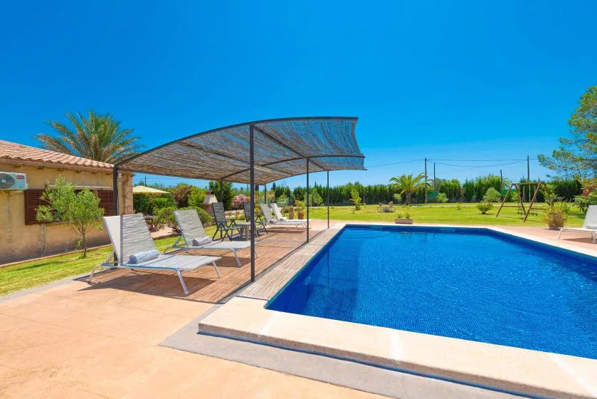 An outdoor swimming pool beside a shaded patio with lounge seating.