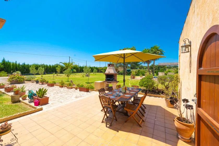 A sunny outdoor patio has a dining table beneath a large umbrella.