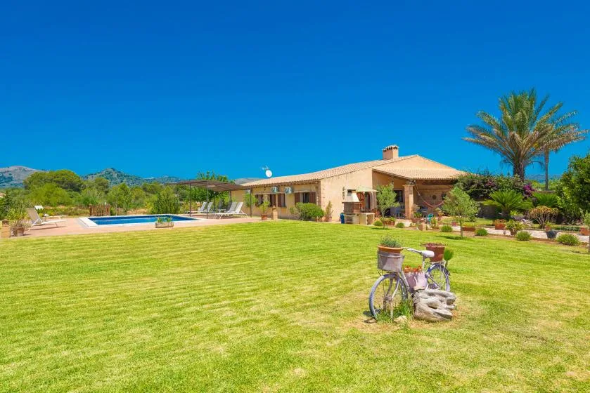A low house sits beyond a broad lawn, with a swimming pool nearby.