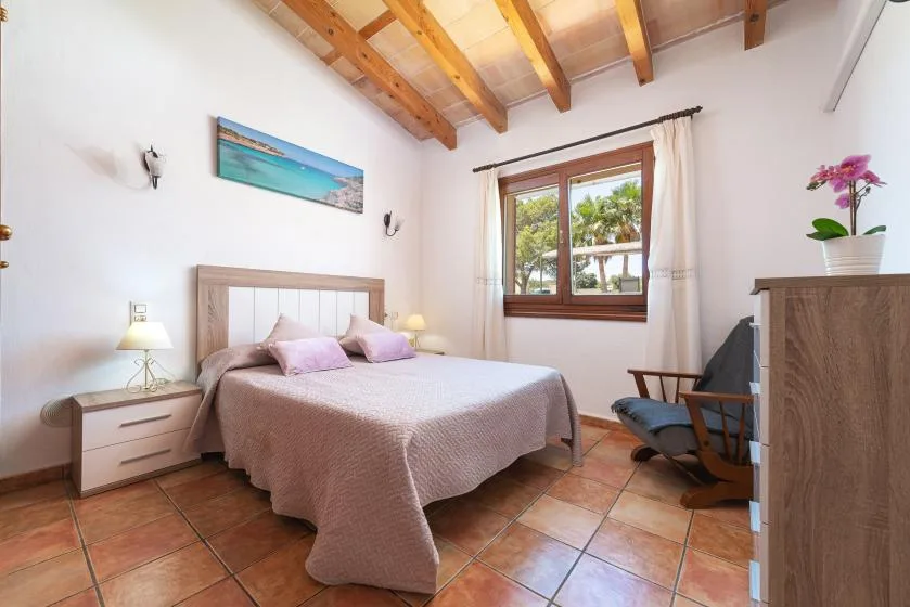 A bedroom with a double bed, bedside tables, and a window overlooking greenery.