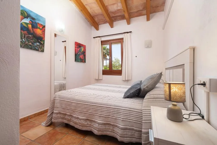 A bedroom with a neatly made bed, bedside lamp, and exposed wooden ceiling beams.