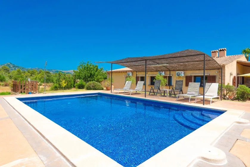 An outdoor swimming pool sits in front of a low building under a clear blue sky.