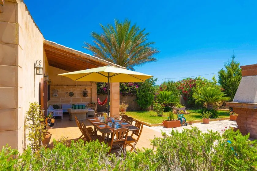 A sunny outdoor patio with dining seating, a canopy, and a landscaped garden.