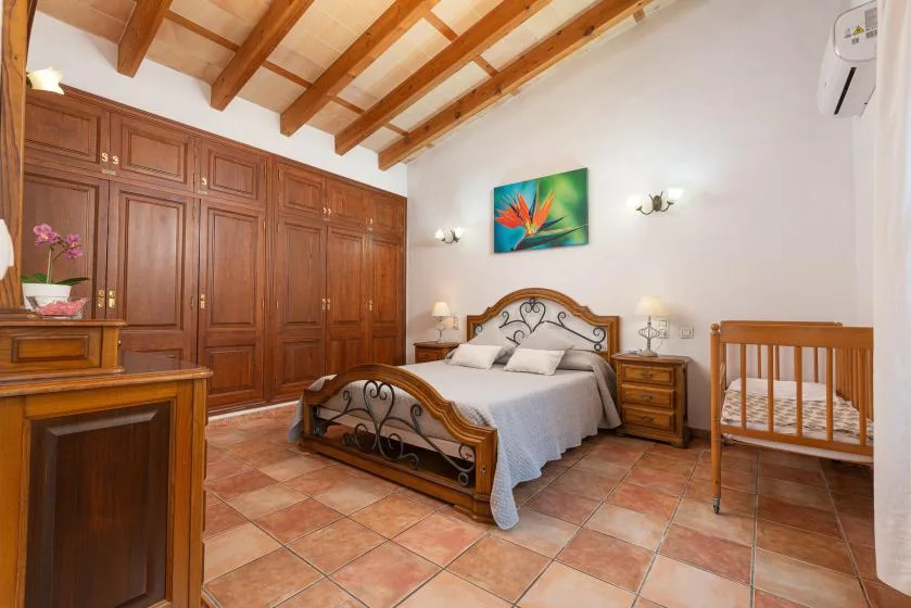 A bedroom with a double bed, wooden wardrobes, and a crib.