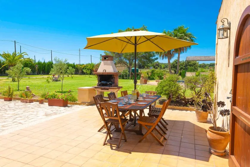 A sunny outdoor dining area has a wooden table beneath a yellow umbrella.