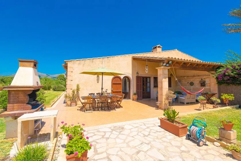 A stone terrace beside a house features outdoor seating and a covered patio.