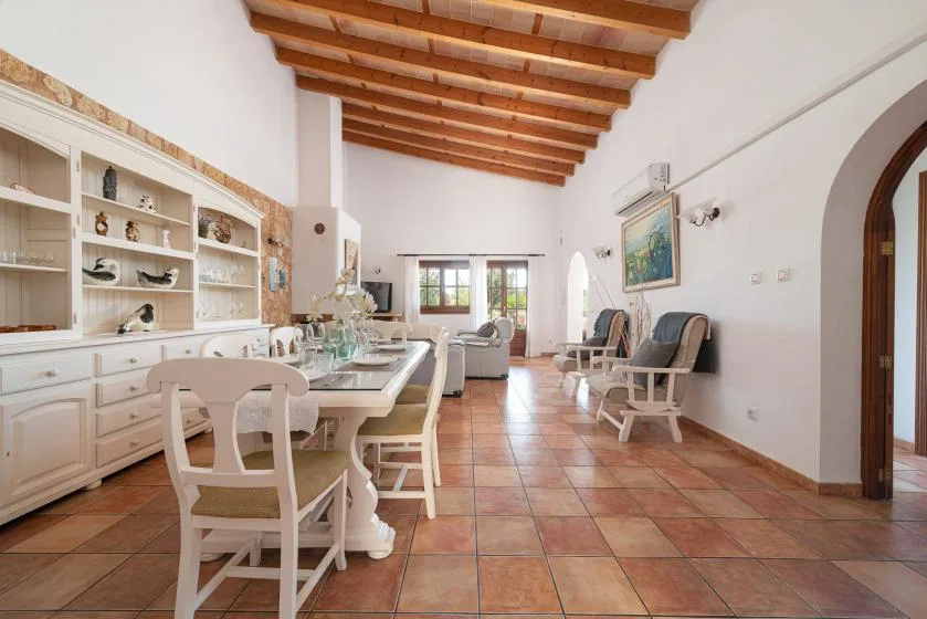 A bright dining and sitting room with a long table and exposed wooden ceiling beams.