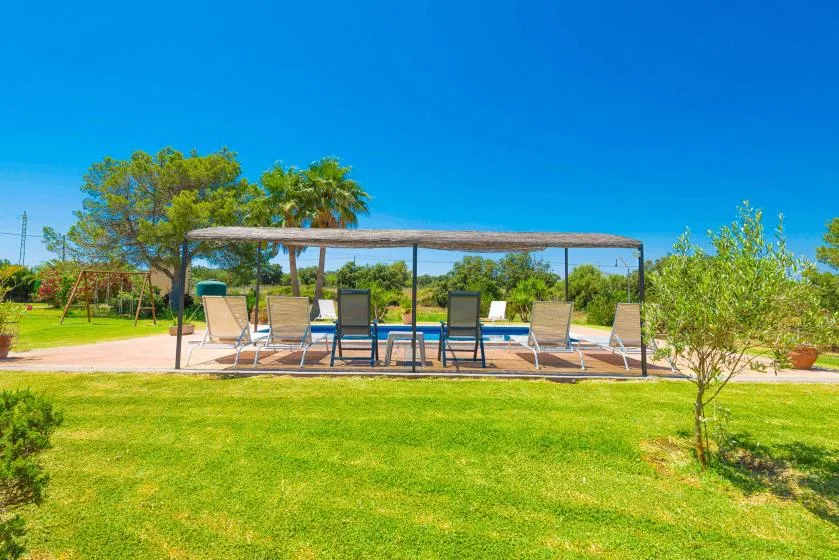 An outdoor seating area sits beneath a shaded pergola beside a lawn.
