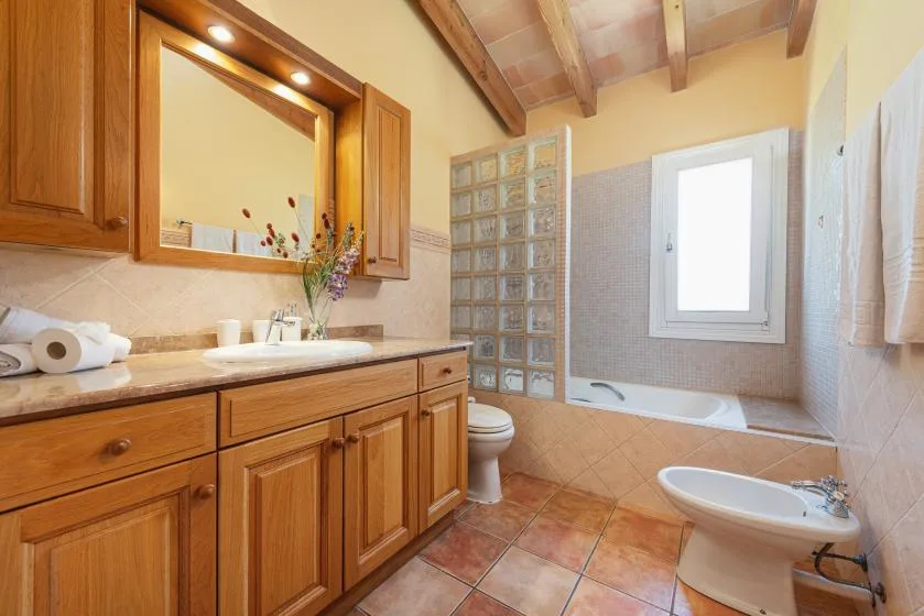 A bathroom with a wooden vanity, bathtub, and glass-block partition.