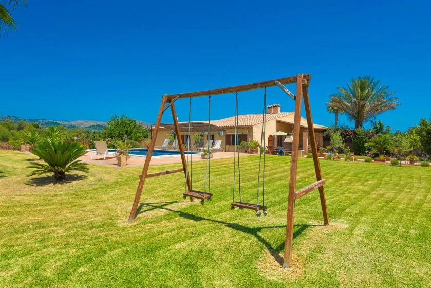 A garden with a wooden swing set on the lawn and a house in the background.